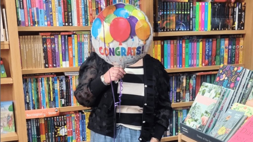 Bridge Books owner Lesley Price holding congratulations balloons for High Street Heroes 2024.